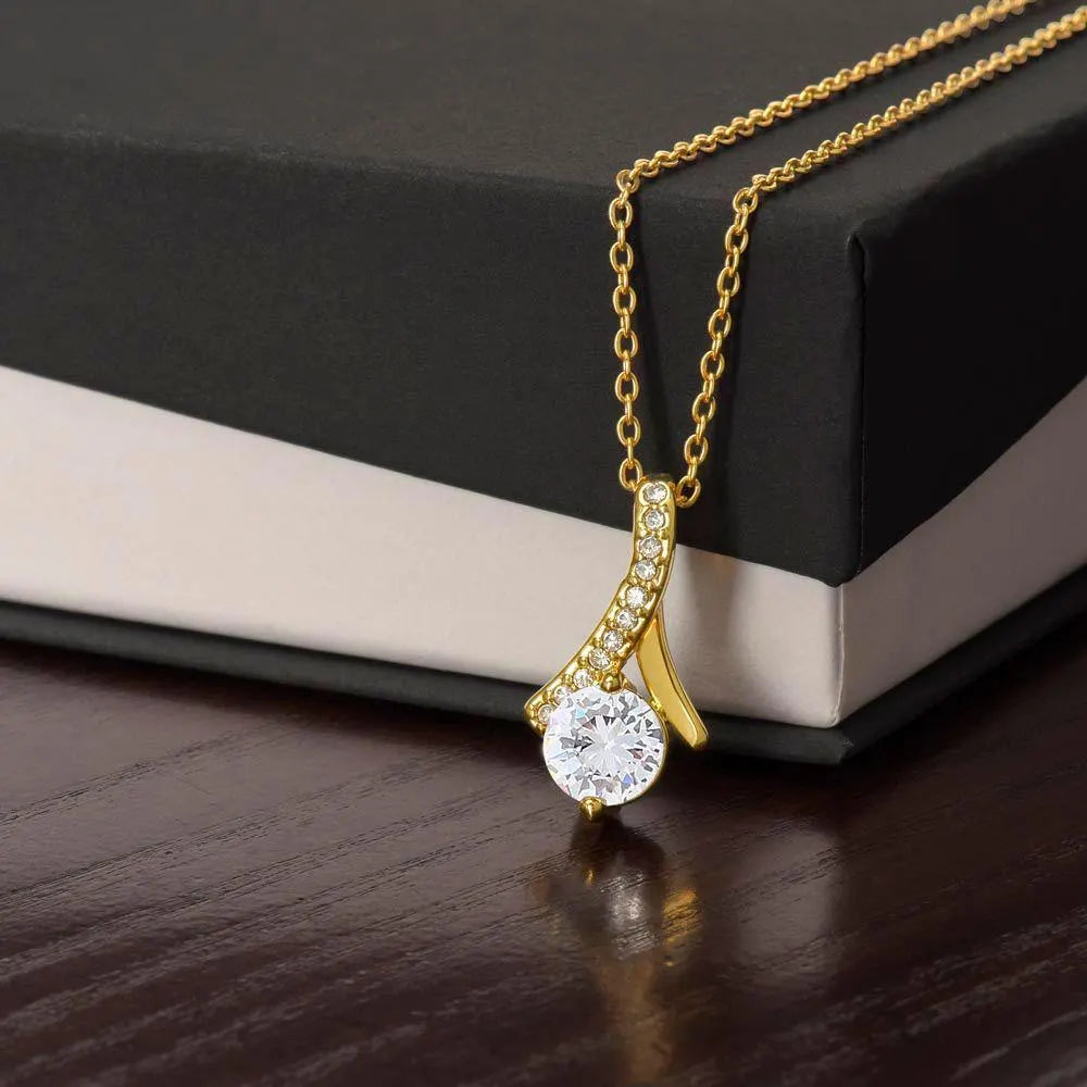 Alluring Beauty necklace in yellow gold finish, resting against a black and cream gift box