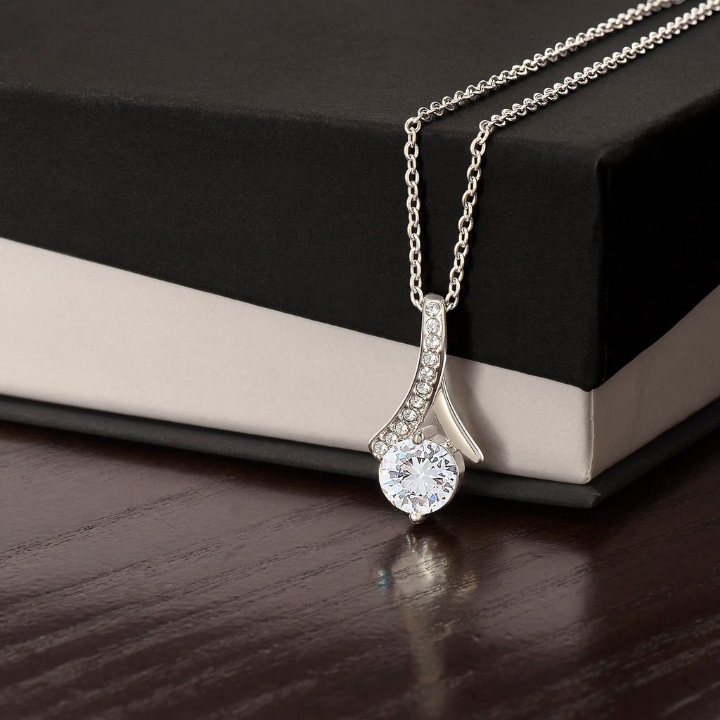 Alluring Beauty necklace in white gold finish, resting against a black and cream gift box