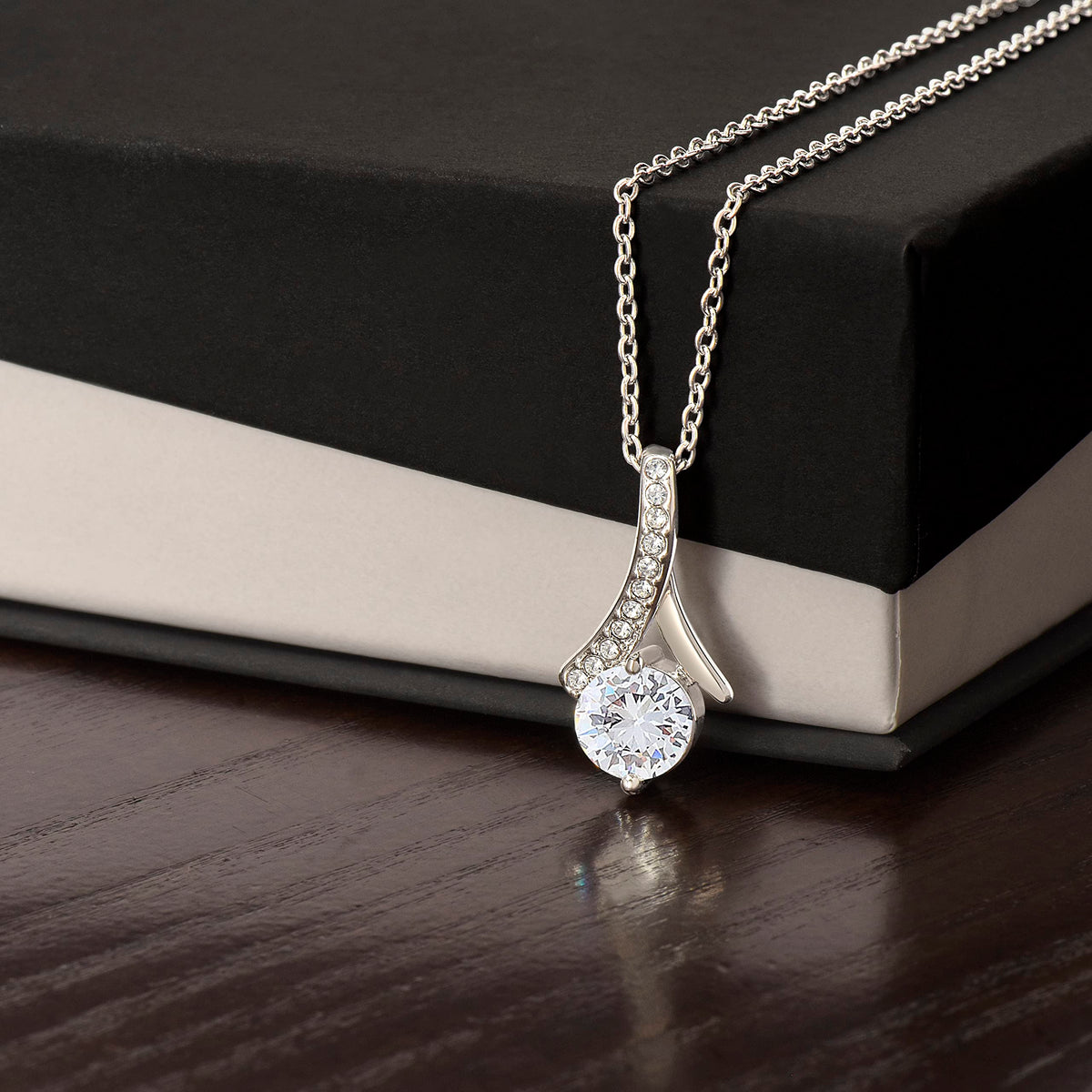 Alluring Beauty necklace in white gold finish, resting against a black and cream gift box
