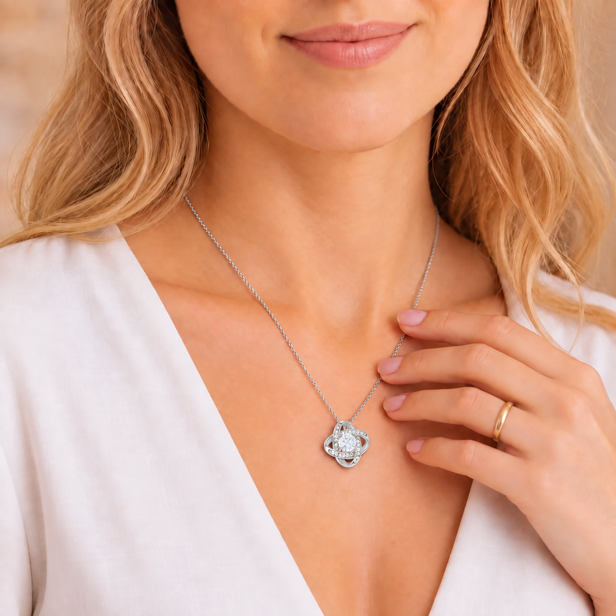 Silver Forever Yours Love Knot necklace worn with an ivory blouse, hand lightly touching the chain